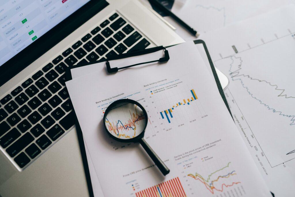 A laptop and papers showing business finances, along with a magnifying glass. This signifies close analysis of business finance data.